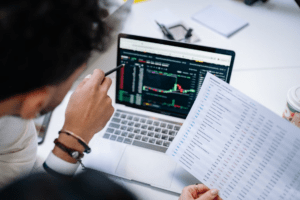 Finance professional reviewing spreadsheet data alongside financial information on a laptop